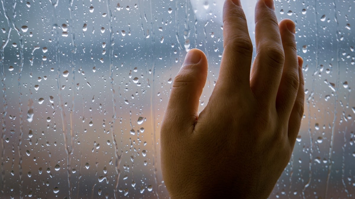 a person's hand on a window with rain drops